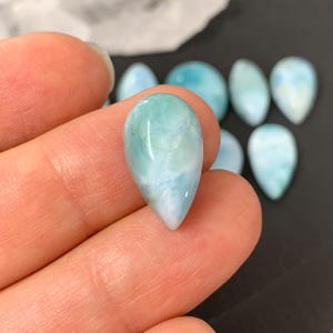 Peut inclure: Une collection de pierres pr&eacute;cieuses cabochon polies en forme de larme, de couleur bleu clair et blanc. Les pierres ont un aspect nuageux et marbr&eacute;.
