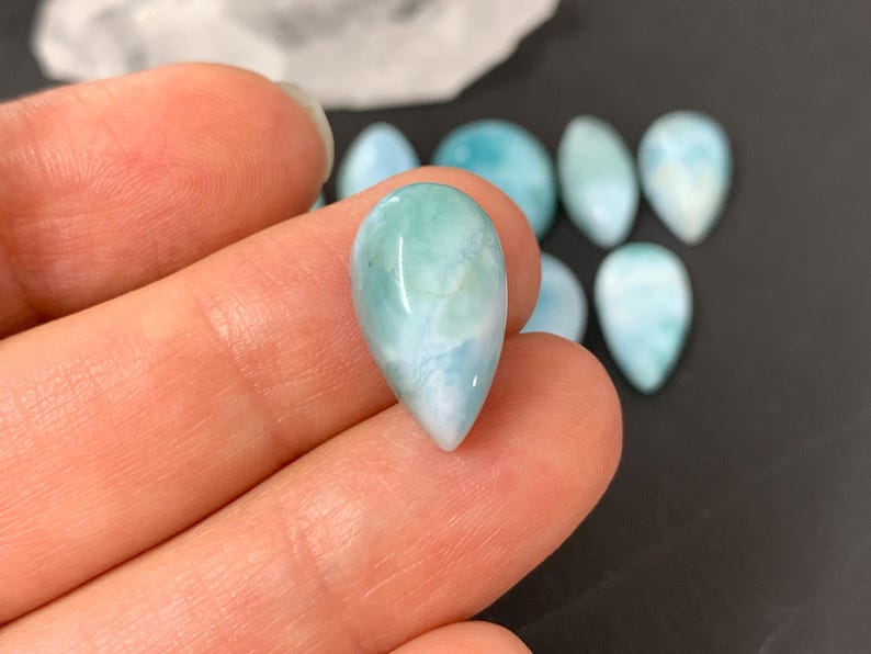 Peut inclure: Une collection de pierres pr&eacute;cieuses cabochon polies en forme de larme, de couleur bleu clair et blanc. Les pierres ont un aspect nuageux et marbr&eacute;.