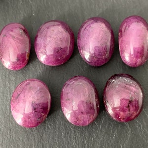 Op de afbeelding: Acht ovale, gepolijste robijn edelstenen. De robijnen zijn diep roze van kleur met een lichte paarse tint. Ze zijn gerangschikt in twee rijen van vier.