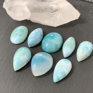 Peut inclure: Une collection de huit cabochons de pierres pr&eacute;cieuses en forme de larme, bleus et blancs. Les cabochons sont lisses et polis, avec une vari&eacute;t&eacute; de motifs tourbillonnants.