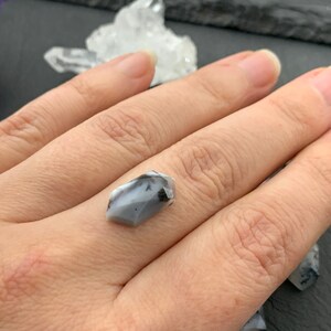 May include: A gray and black gemstone with a pointed shape, held in a hand.