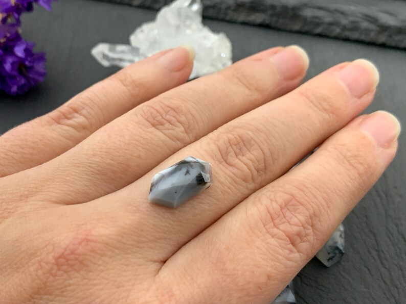 May include: A gray and black gemstone with a pointed shape, held in a hand.