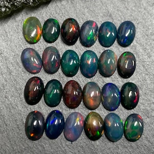 May include: A collection of 18 oval-shaped black opals with iridescent green, blue, and red flashes. The opals are arranged in three rows of six.