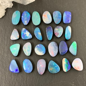 May include: A collection of polished opal gemstones in various shapes and sizes, showcasing a spectrum of colors including blues, greens, and pinks. The opals are arranged on a dark, textured surface, highlighting their iridescent qualities.
