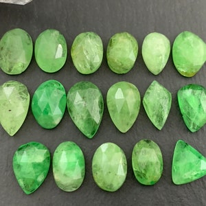 May include: A collection of 15 green gemstone cabochons in various shapes and sizes. The stones are faceted and have a translucent appearance.