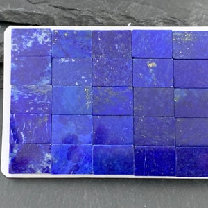 May include: A rectangular arrangement of deep blue lapis lazuli tiles with gold flecks, set within a white border. The tiles are arranged in a grid pattern, showcasing the natural variations in color and texture of the stone.