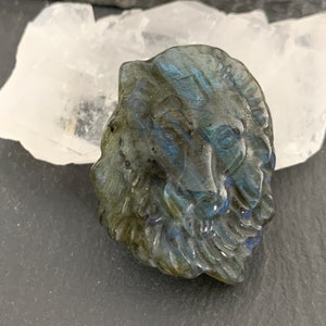 May include: A carved labradorite stone lion head pendant with iridescent blue and green colors.