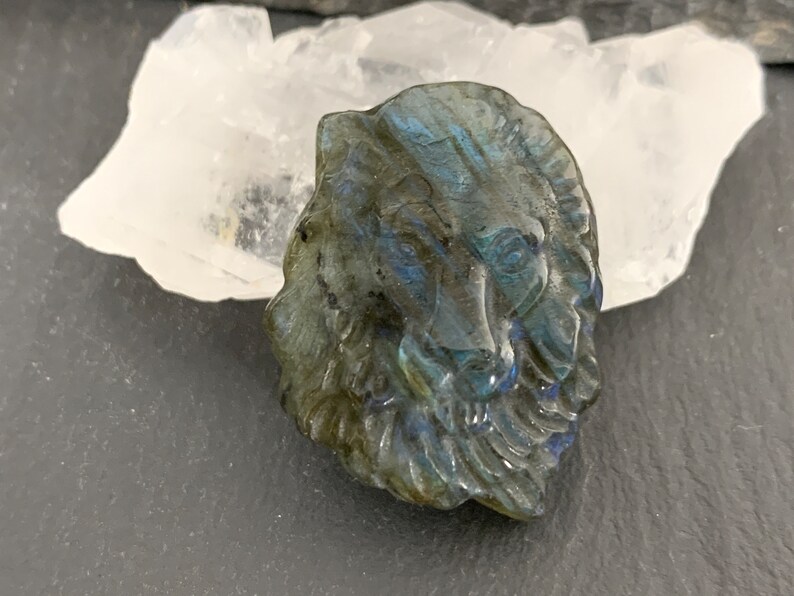May include: A carved labradorite stone lion head pendant with iridescent blue and green colors.