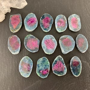 May include: A collection of 14 pink and blue gemstone cabochons. The cabochons are all different shapes and sizes, but they are all cut in a similar style. They are all polished and have a smooth, shiny finish.