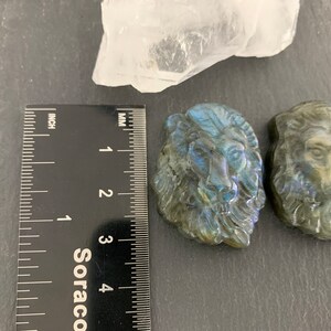 May include: Three carved labradorite lion head sculptures, each approximately 3 cm in size, with iridescent blue and green colors.