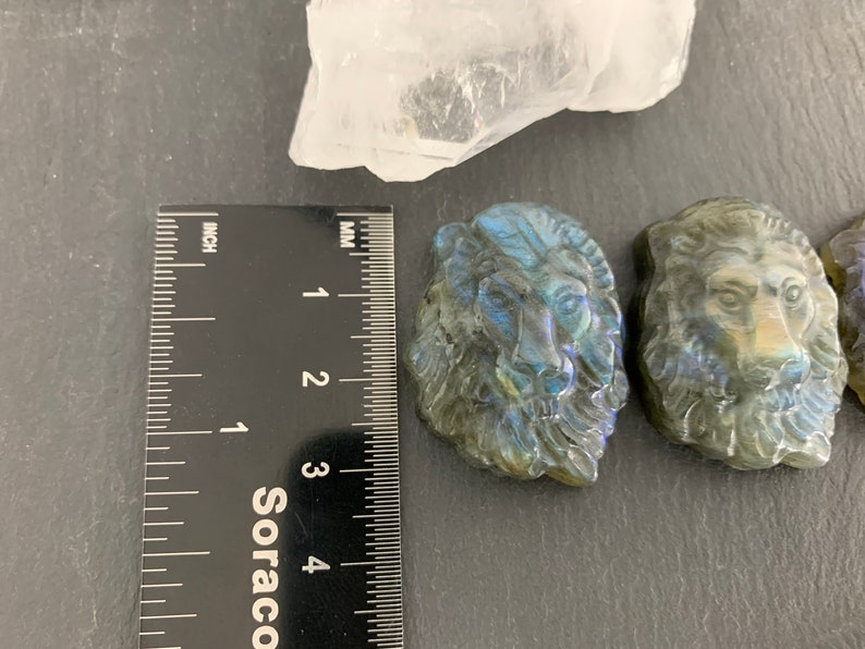 May include: Three carved labradorite lion head sculptures, each approximately 3 cm in size, with iridescent blue and green colors.