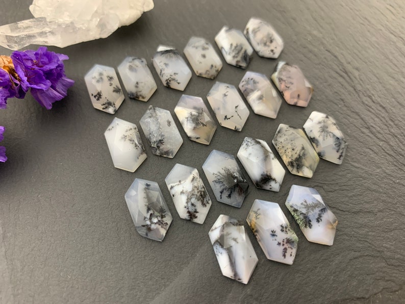 May include: A collection of 18 white and black dendritic agate cabochons in a hexagonal shape. The cabochons are arranged in rows on a dark gray surface.