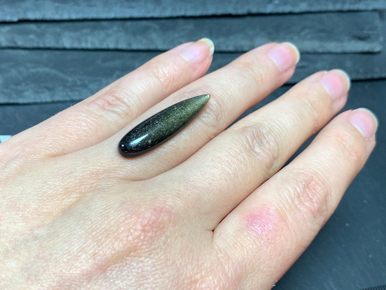 以下が含まれることがあります： 黒と緑の色合いの、涙の形をした金色の光沢のある黒曜石のカボションです。
