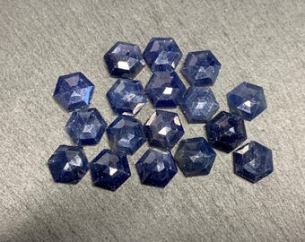 以下が含まれることがあります： 六角形の形状と深い青色の15個のファセットカットされたサファイアジェムストーンのコレクション。ジェムストーンは、灰色の背景にクラスター状に配置されています。
