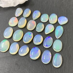 May include: A collection of 20 oval-shaped, iridescent opal gemstones. The opals are a milky white color with flashes of blue, green, and pink.