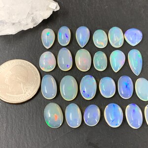 May include: A collection of 18 iridescent opal cabochons in various shapes and sizes. The opals are a milky white color with flashes of blue, green, and pink.