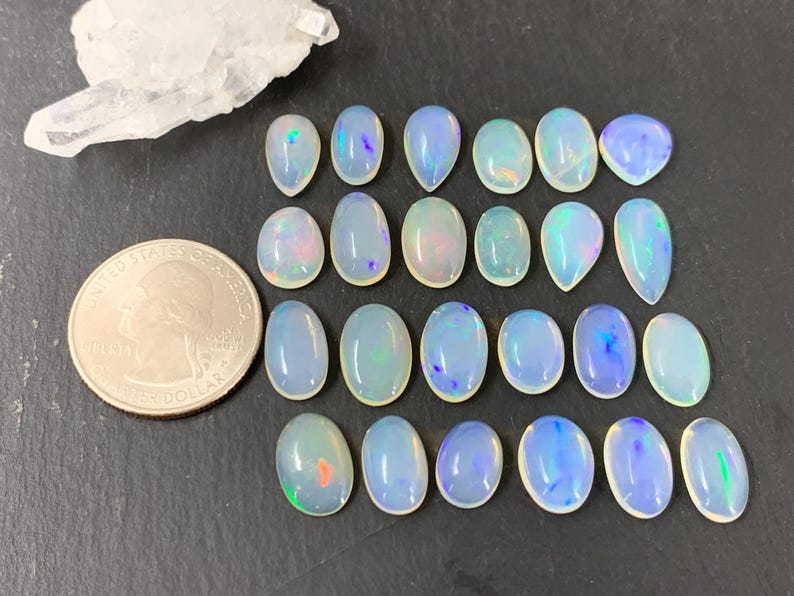 May include: A collection of 18 iridescent opal cabochons in various shapes and sizes. The opals are a milky white color with flashes of blue, green, and pink.