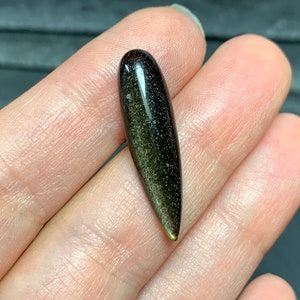 以下が含まれることがあります： 尖った先端を持つ濃い緑と黒の宝石のカボション。宝石はキラキラと虹色に輝く仕上げになっています。