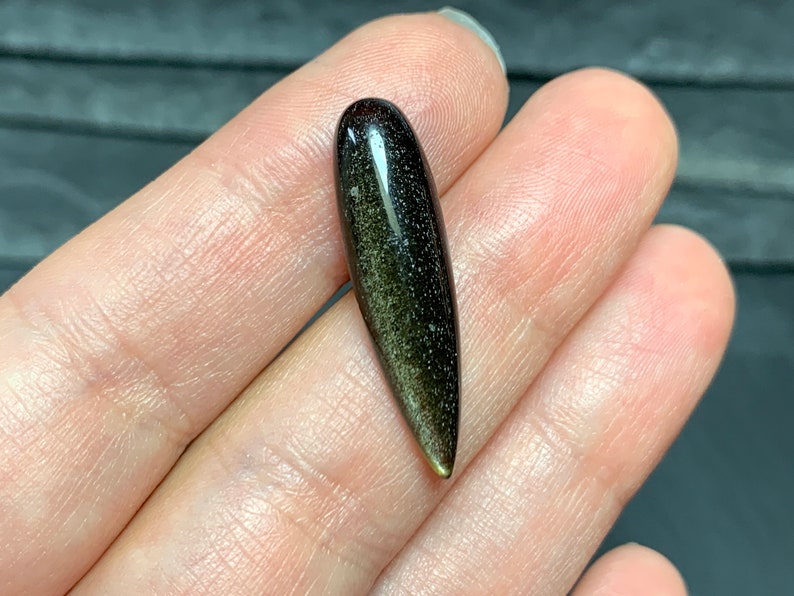 以下が含まれることがあります： 尖った先端を持つ濃い緑と黒の宝石のカボション。宝石はキラキラと虹色に輝く仕上げになっています。