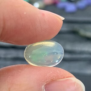 May include: A pale green and white oval opal gemstone with a slight iridescent sheen.