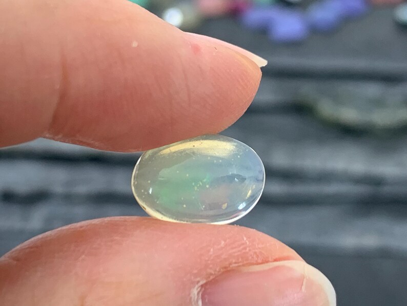 May include: A pale green and white oval opal gemstone with a slight iridescent sheen.