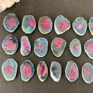 May include: Assortment of 15 pink and blue gemstone cabochons. The cabochons are oval and round shaped and have a smooth, polished finish.