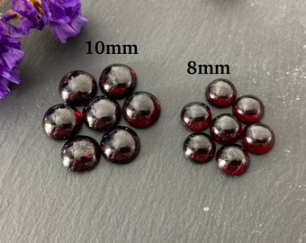 May include: Two groups of round, dark red glass cabochons. The group on the left is labeled "10mm" and the group on the right is labeled "8mm".