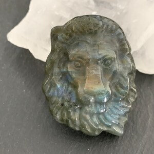 May include: A carved labradorite lion head pendant with iridescent blue and green colors.