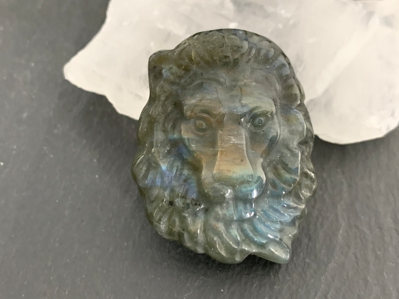 May include: A carved labradorite lion head pendant with iridescent blue and green colors.