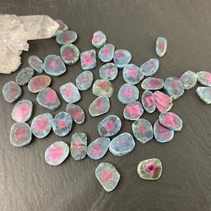 May include: A collection of 25 loose, natural, green and pink ruby gemstone cabochons. The cabochons are irregularly shaped and have a smooth, polished surface.