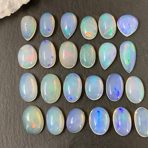 May include: A collection of 18 oval and teardrop shaped opal cabochons. The opals are a milky white color with iridescent flashes of blue, green, and pink.