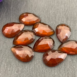 May include: Eight pear-shaped, faceted, brown gemstones. The stones are arranged in a cluster on a dark gray surface.