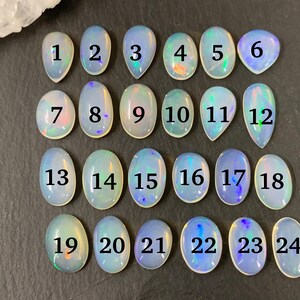 May include: Twenty-four iridescent opal cabochons, each with a number from 1 to 24, arranged in four rows of six. The cabochons are oval-shaped and have a milky white color with flashes of rainbow.
