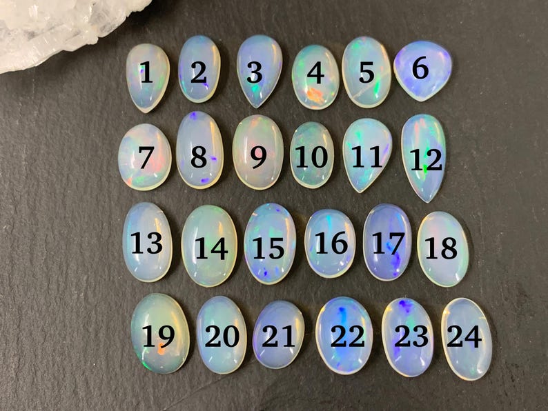 May include: Twenty-four iridescent opal cabochons, each with a number from 1 to 24, arranged in four rows of six. The cabochons are oval-shaped and have a milky white color with flashes of rainbow.
