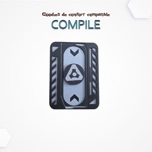 May include: A black and gray phone accessory with the word "COMPILE" in teal. The accessory has a central circular element with a geometric design and two directional arrows. The top of the image has the text "Goodies de confort compatible".