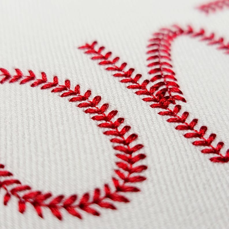 May include: Close-up of white fabric with red baseball stitching forming the word "ON". The red stitching is detailed and prominent against the white background, creating a textured effect. The image evokes a sports theme.