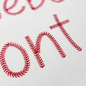 May include: Close-up of white fabric with red baseball-style stitching forming the word "Sweet On". The stitching is detailed and creates a textured effect against the smooth white background. The design is likely for sports fans.