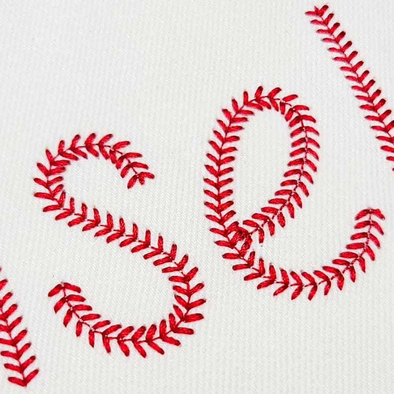 May include: White fabric with the word "SOLD" embroidered in red thread. The letters are stylized with a baseball stitch design, creating a sporty and handcrafted aesthetic. The image is a close-up, highlighting the texture.