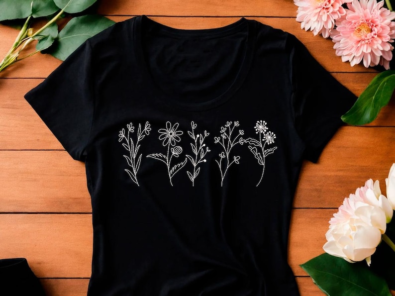 May include: Black t-shirt featuring a white embroidered floral design. The design includes various stylized flowers and stems. The shirt is made of a soft material and has a crew neck.