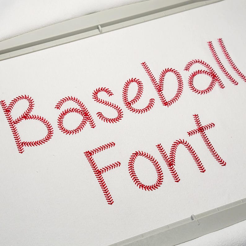 May include: Close-up of the words "Baseball Font" embroidered in red thread on white fabric. The letters are designed to resemble baseball stitching. The image is framed by a white embroidery hoop.