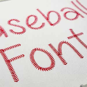 May include: White fabric with red embroidered text that reads "Baseball Font". The letters are designed to resemble the stitching on a baseball, with a repeating pattern of red thread.