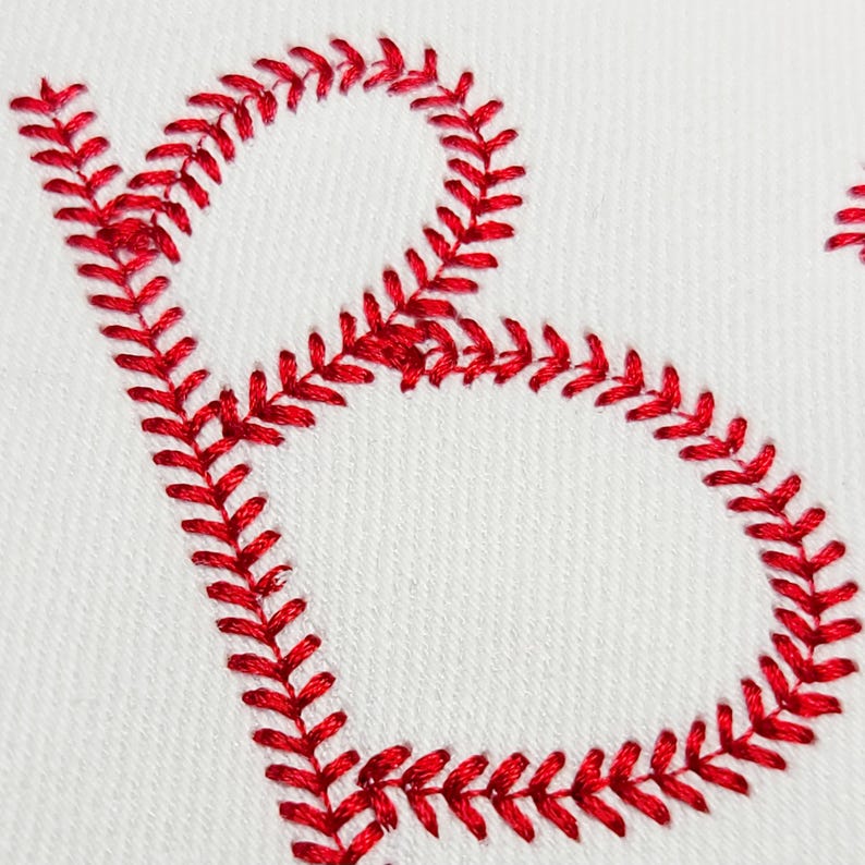 May include: Close-up of a white fabric with a red embroidered letter "B". The letter is formed with a baseball stitch, a decorative stitch that resembles the seams of a baseball. The embroidery is in a vibrant red color.