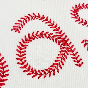 May include: Close-up of white fabric with red embroidered baseball stitching. The stitching is in a repeating pattern, creating a textured effect. The image focuses on the details of the embroidery.