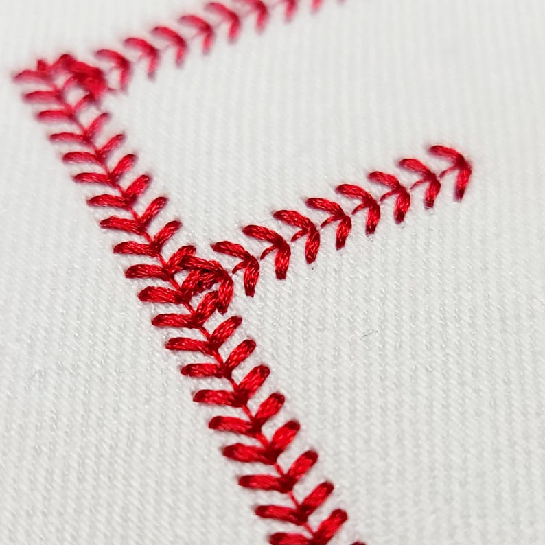 May include: Close-up of a white fabric with red embroidery. The embroidery forms a V-shape, with each side of the V outlined by a series of small, red stitches. The stitches are evenly spaced and create a textured effect.