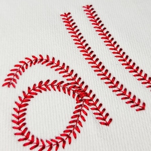 May include: Close-up of white fabric with red stitching in a baseball-inspired design. The stitching forms the letters "all" in a decorative style, with the "a" in a circular shape.