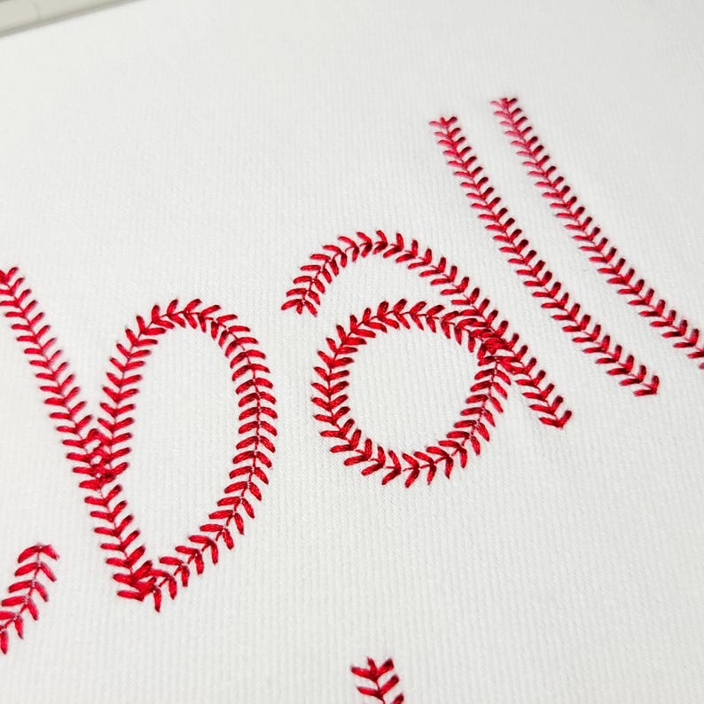 May include: White fabric with the word "baseball" embroidered in red thread. The letters are stylized to resemble the stitching on a baseball. The image is a close-up of the embroidery.