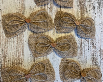 May include: Five burlap bows with wooden heart accents. The bows are arranged in a pyramid shape on a white wooden background.
