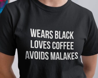 May include: A black t-shirt with white text that reads "Wears Black Loves Coffee Avoids Malakes".