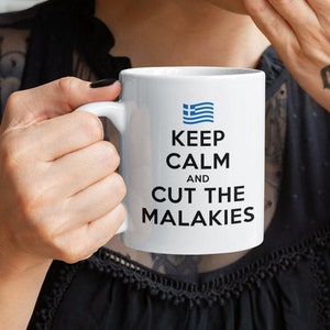 May include: White ceramic mug with a black handle. The mug has a blue and white Greek flag and the text "Keep Calm and Cut the Malakies".