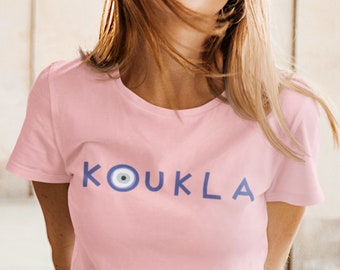 May include: A pink t-shirt with a blue and white evil eye graphic and the text "KOUKLA" printed on the front.